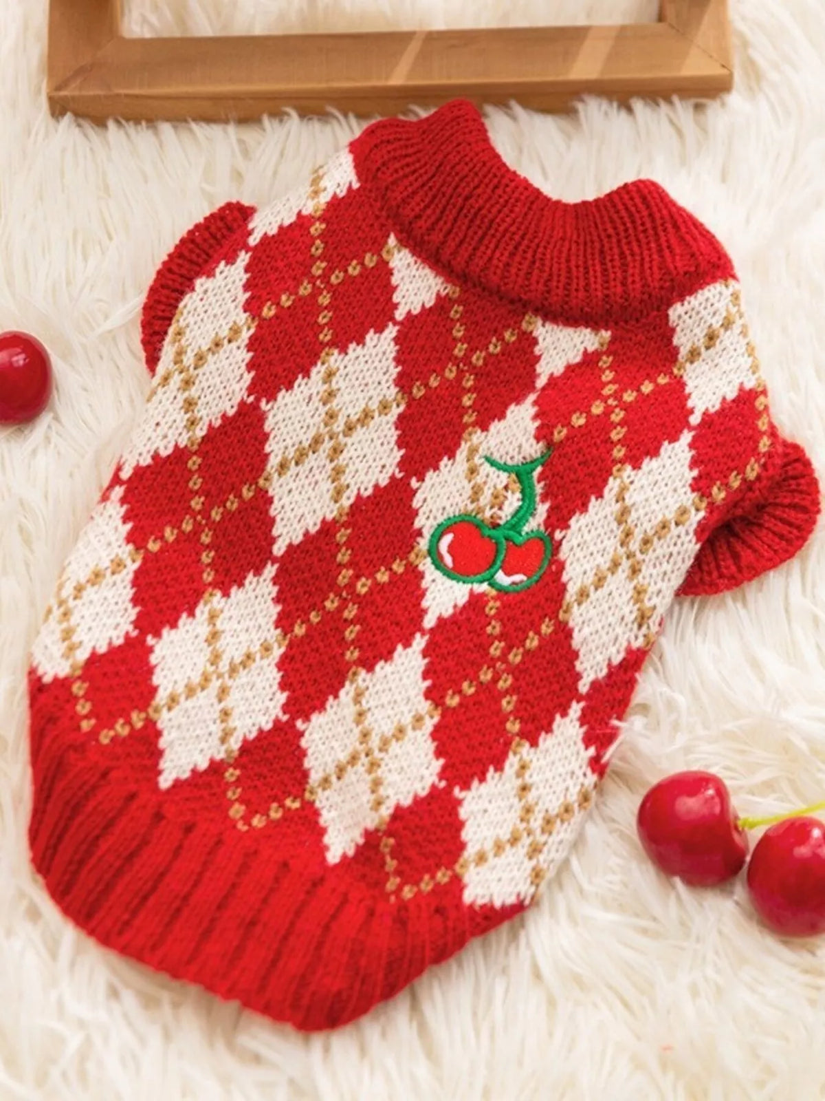 Red-and-cream argyle pet sweater with a cherry applique, shown flat.
