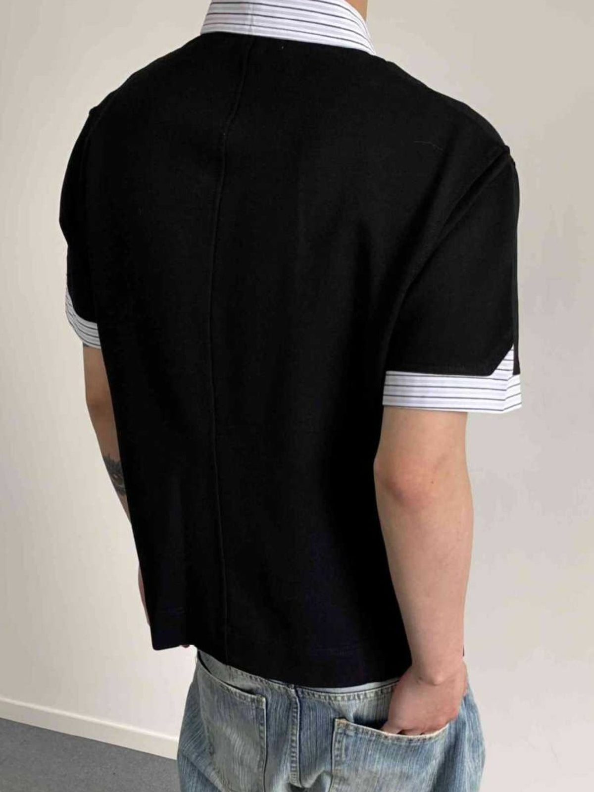 Back of the black polo showing the plain body and striped collar and sleeve trim.