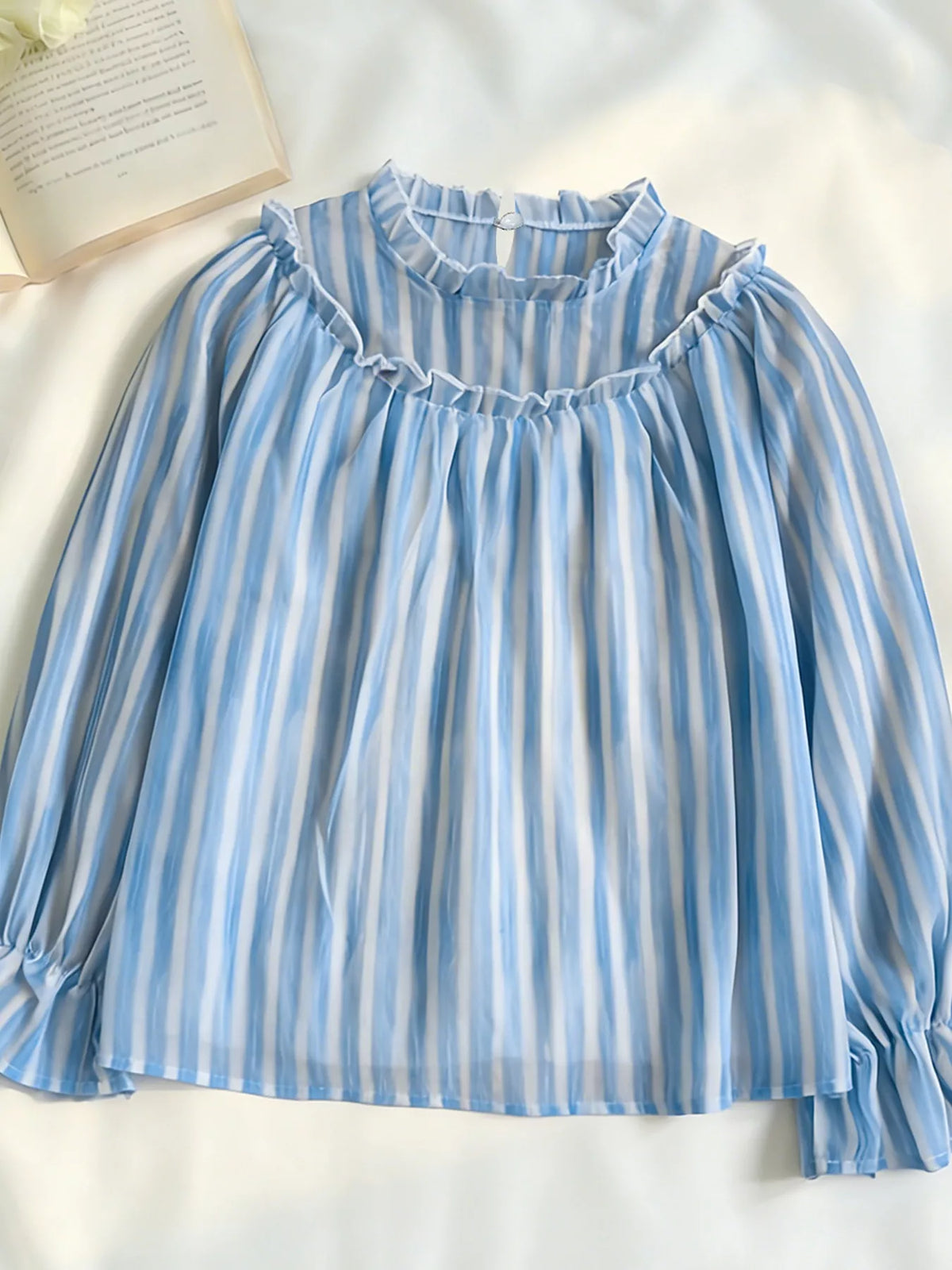 Blue and white striped blouse laid flat, showing ruffled neckline and long sleeves