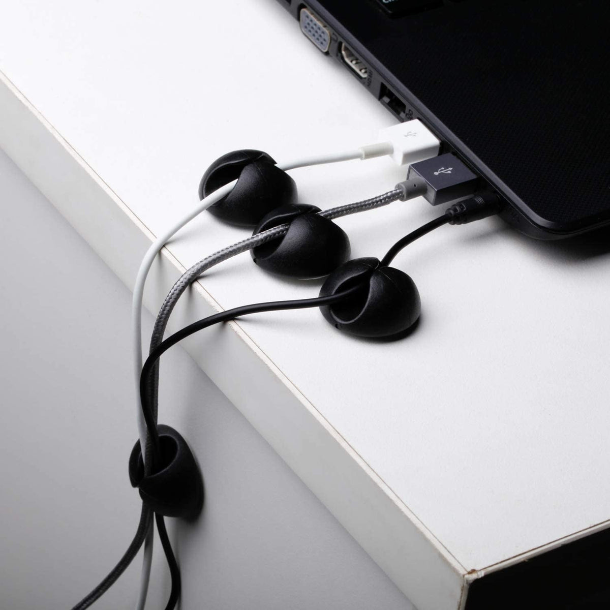 Black cable holders guiding cables beside a laptop; cables and laptop not included