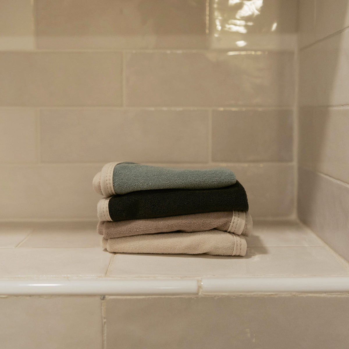 Four folded terry washcloths stacked on a tiled ledge.