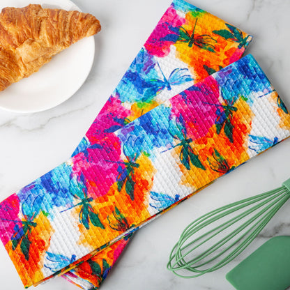 Dragonflies kitchen-towel pair on a counter; food and utensils are styling props.