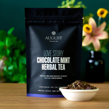 August Uncommon Tea Love Story chocolate-mint herbal tea 15-cup pouch beside a bowl of loose blend