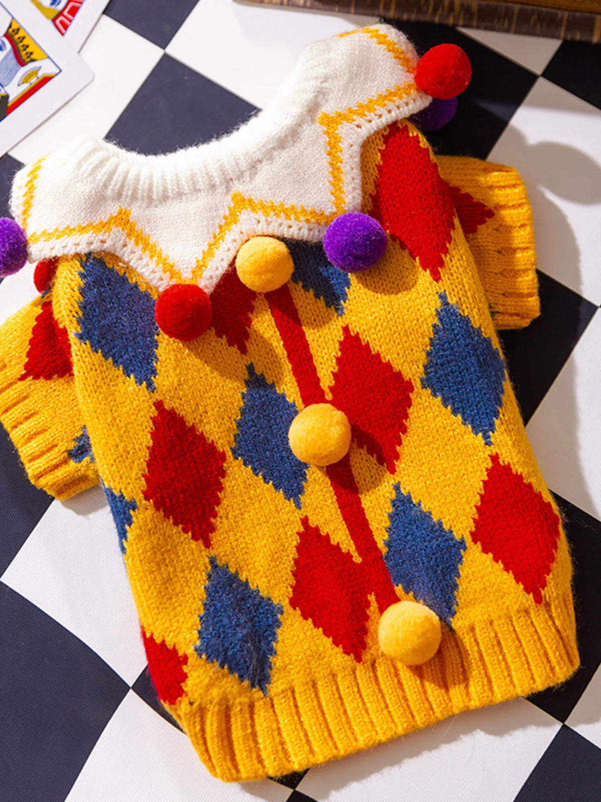 Yellow diamond-pattern pet sweater with colorful pom-pom details, shown flat.