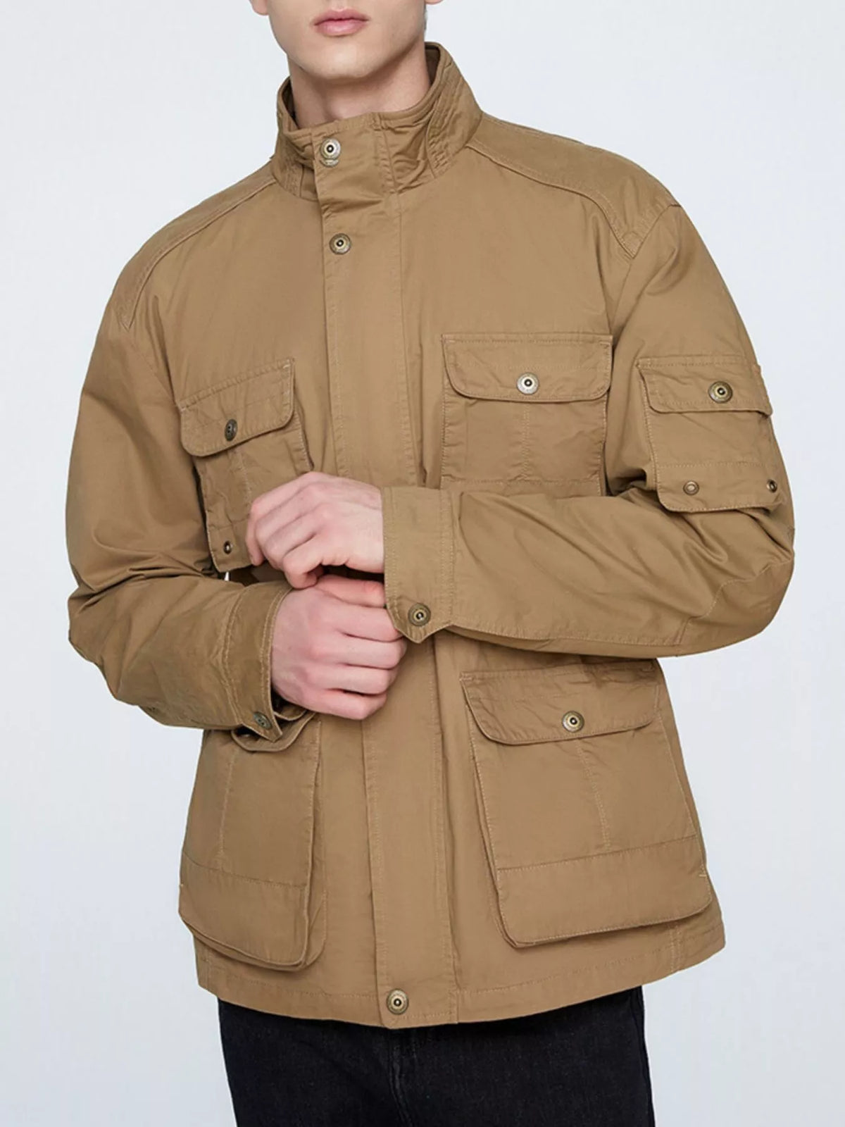 Khaki multi-pocket men's jacket shown fastened from the front with the model adjusting a cuff; trousers are not included.