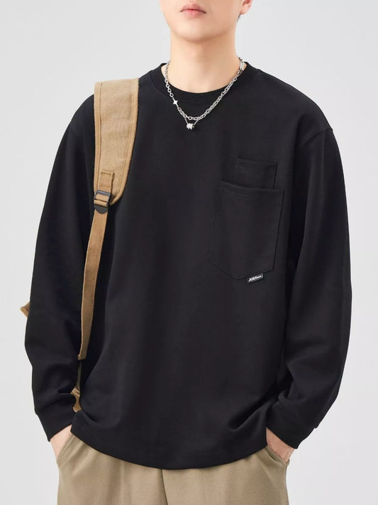 Men's black long-sleeve sweatshirt with layered chest-pocket detail, styled with a tan bag