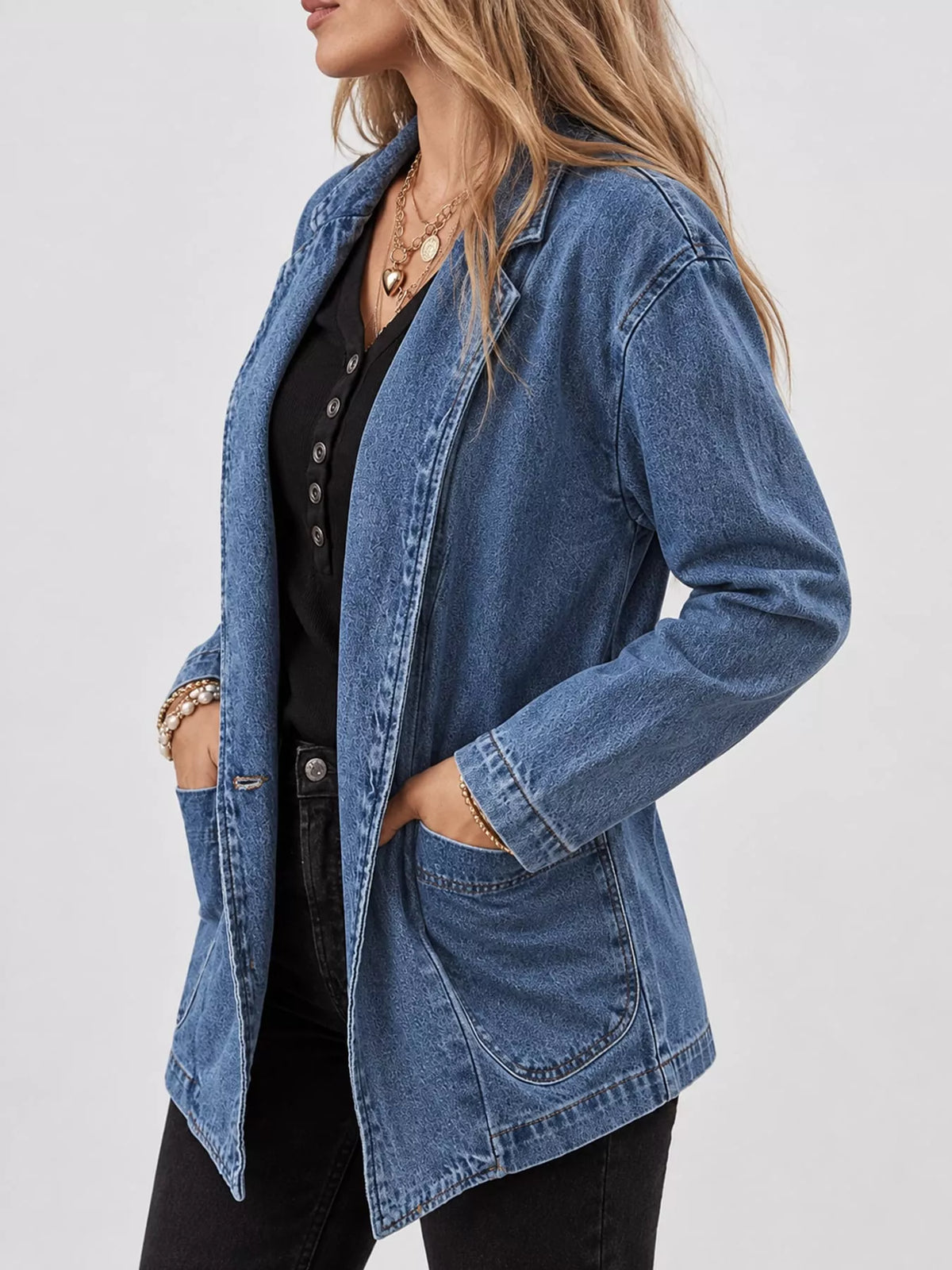 Side view of the medium blue denim blazer showing its collar, long sleeves and front patch pockets