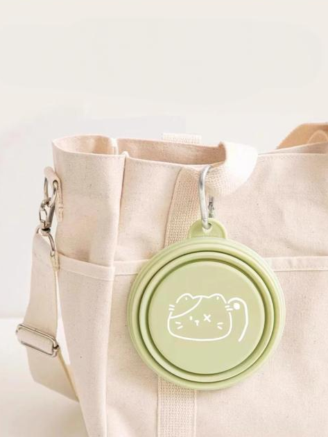 Green folded travel item clipped to a beige tote bag in a carrying illustration; bag is not included.