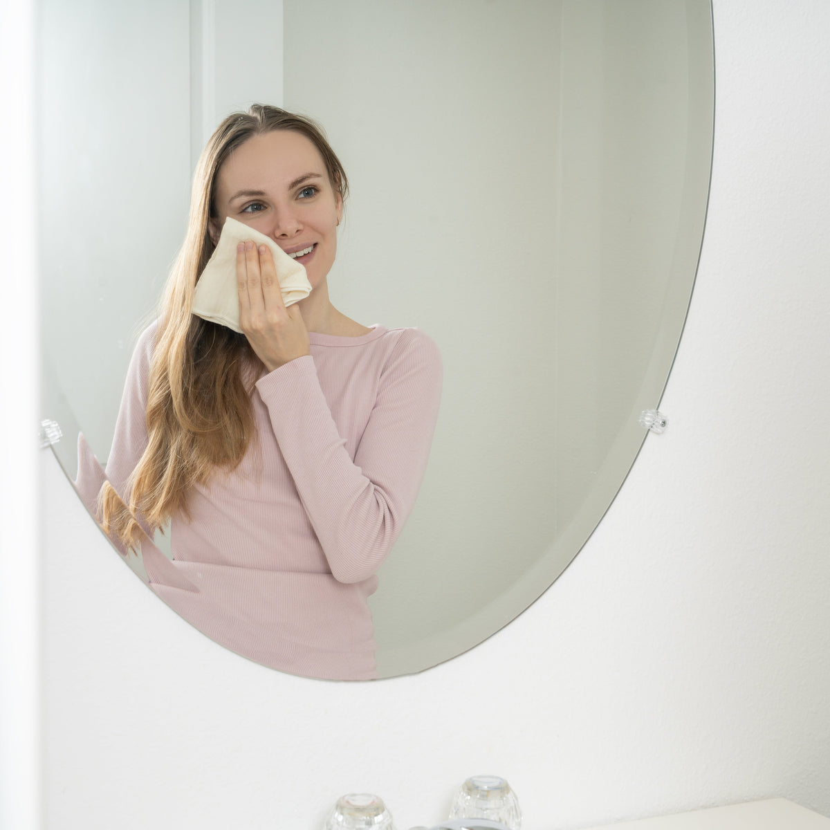 Adult using a cotton cloth on her cheek beside a mirror