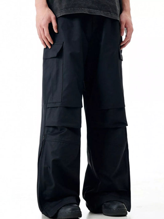 Front view of black loose-fit cargo trousers on a model, showing flap thigh pockets and full-length wide legs.