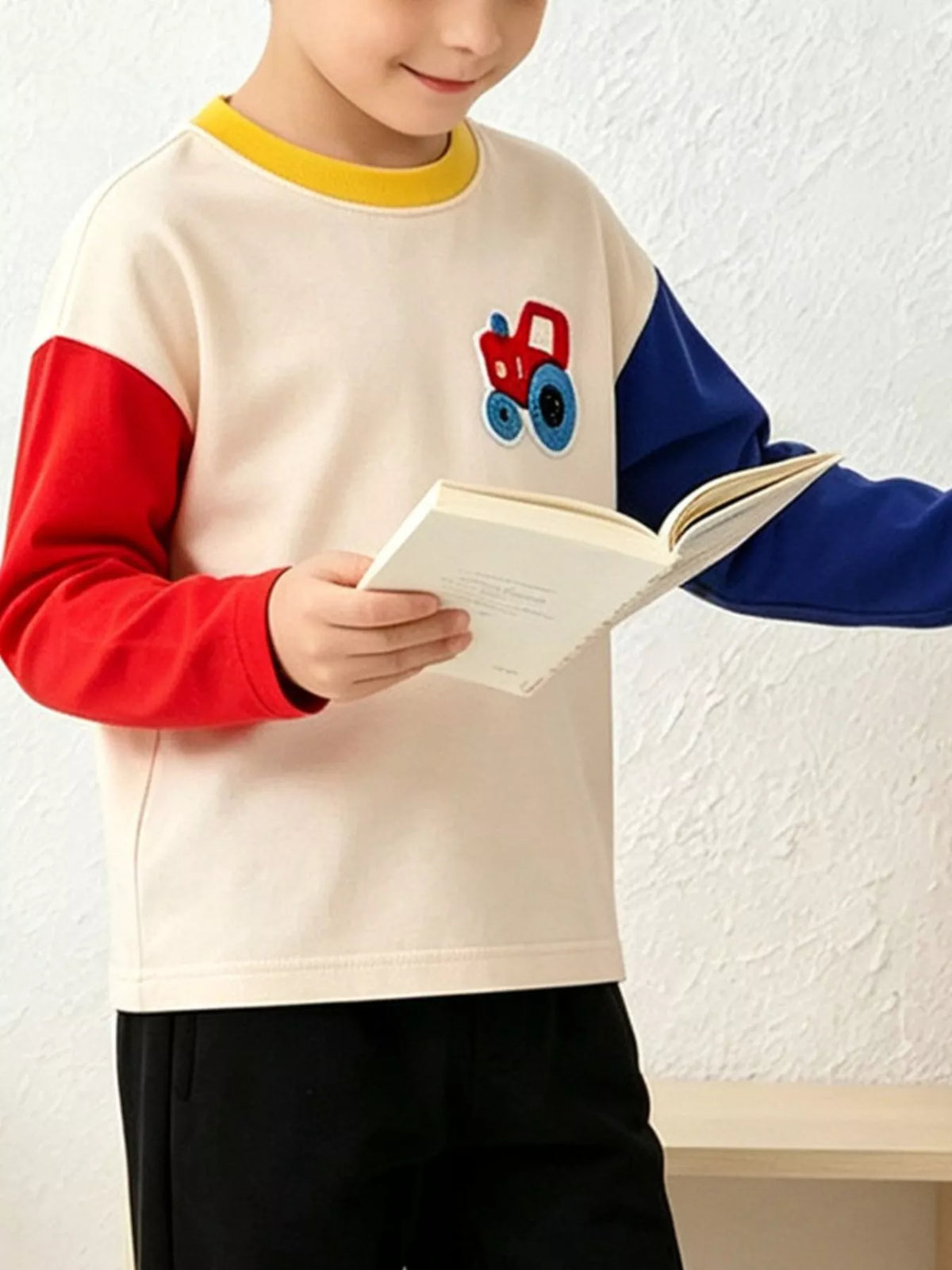 Children's tractor applique sweatshirt shown while reading; book and trousers are styling props and are not included.