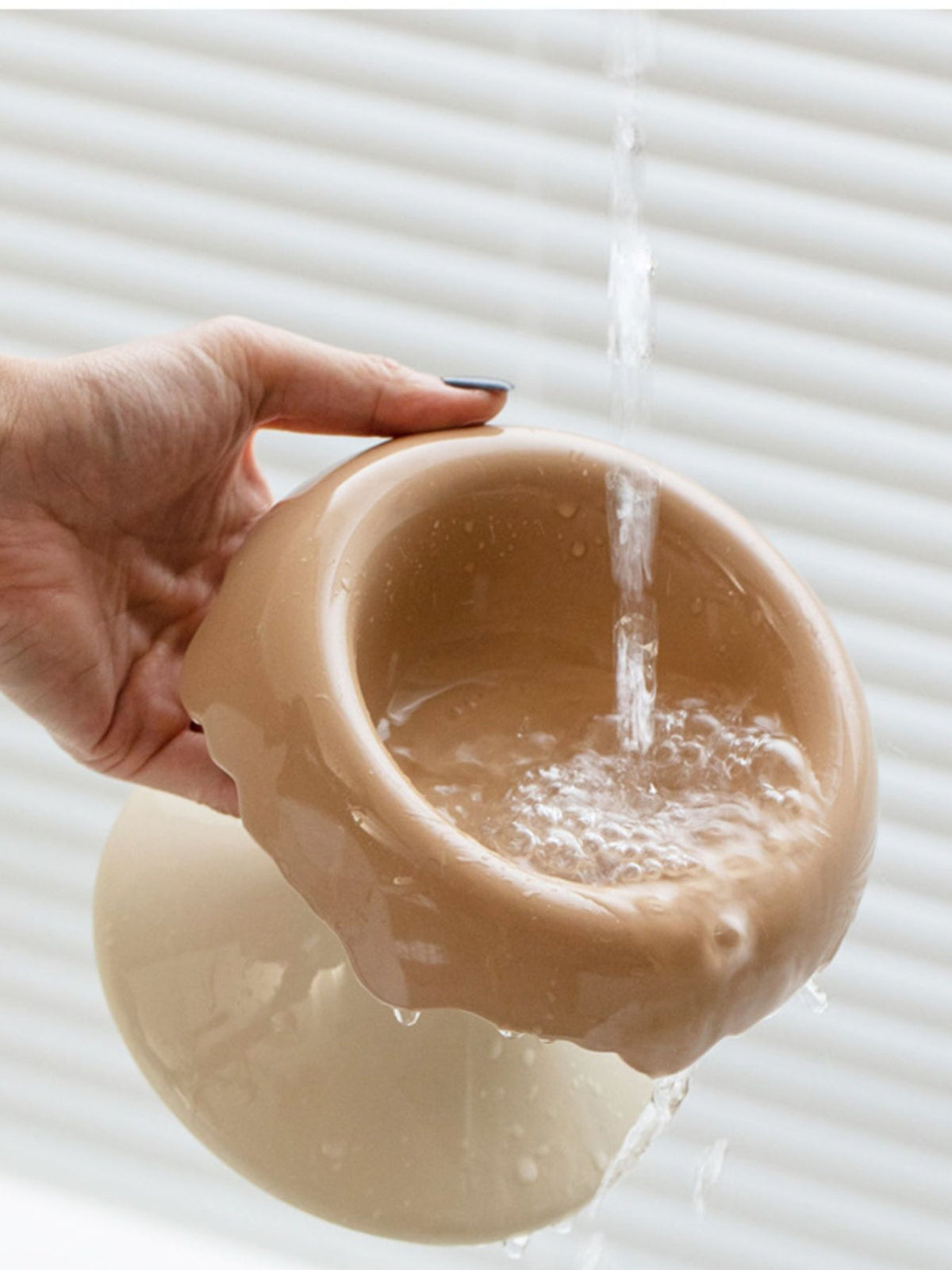 Camel-and-white elevated bowl shown being rinsed with water.
