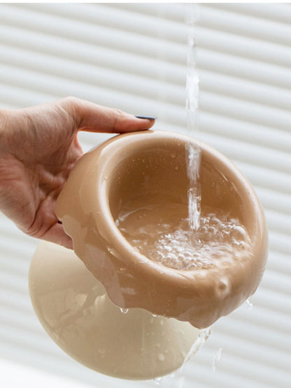 Camel-and-white elevated bowl shown being rinsed with water.