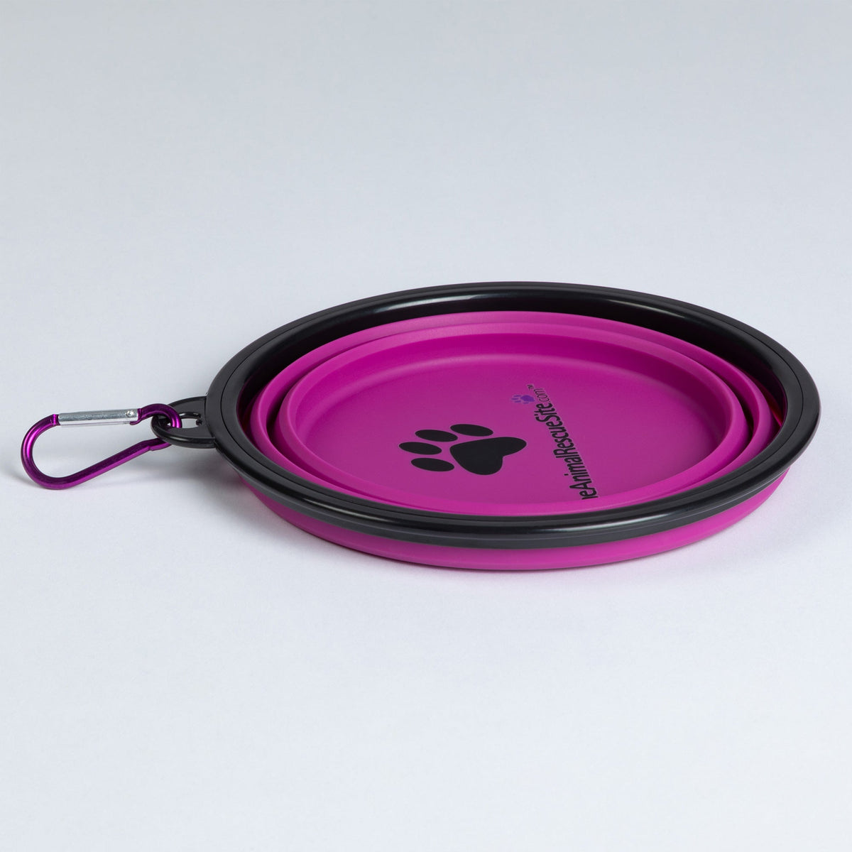 Pink pet bowl folded flat, with black rim, matching carabiner and printed paw design.