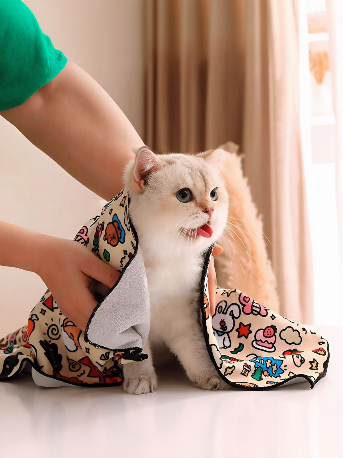 White cat wrapped in a colorful cartoon-print pet bath towel, held gently at its sides.