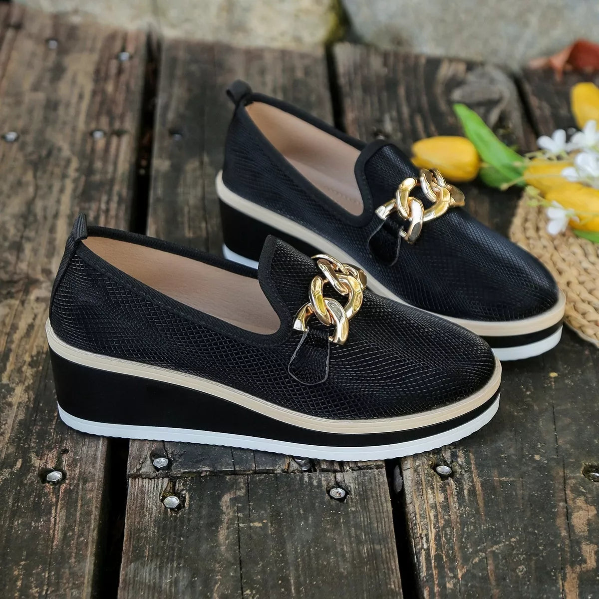 Black loafers displayed on a wooden surface beside flowers; props are not included.
