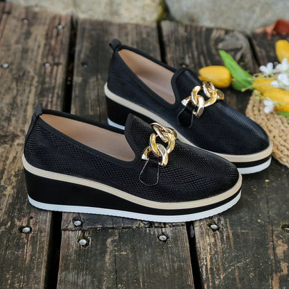 Black loafers displayed on a wooden surface beside flowers; props are not included.