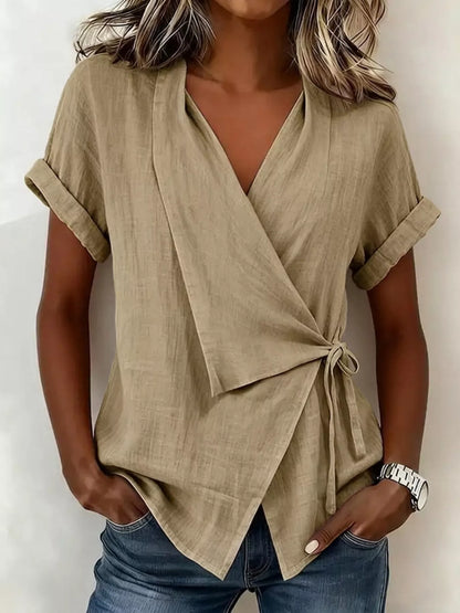 Beige wrap top on a model, front view with a V-neck, cuffed short sleeves, side tie and overlapping hem.