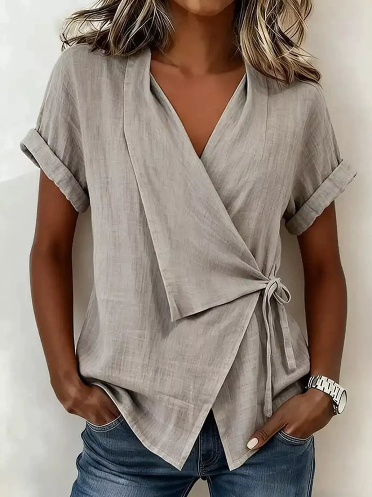 Gray wrap top on a model, front view showing a V-neck, cuffed short sleeves, side tie and overlapping pointed hem.