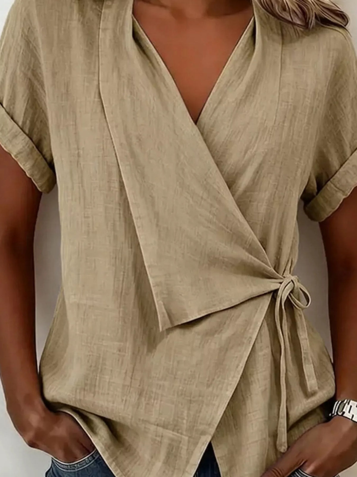 Beige wrap top front detail showing the side tie, cuffed sleeves and overlapping pointed hem.
