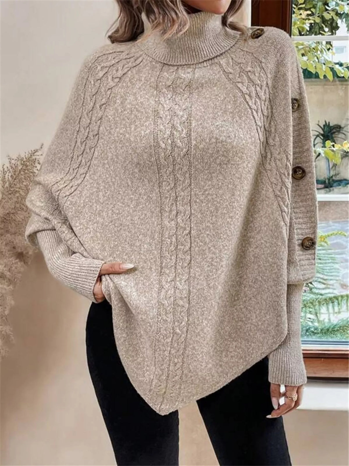 Warm beige/oatmeal cable-knit turtleneck cape sweater. Front view emphasizing cable-knit front and sleeve buttons. Styling accessories are not included.