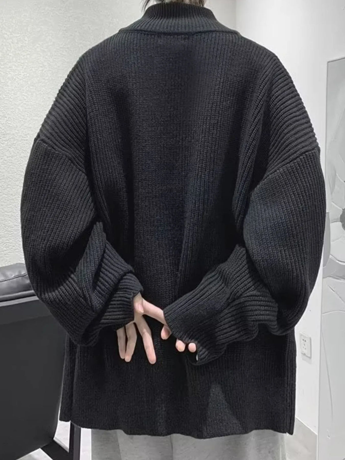 Back view of the black oversized ribbed cardigan, showing its dropped shoulders and long sleeves.