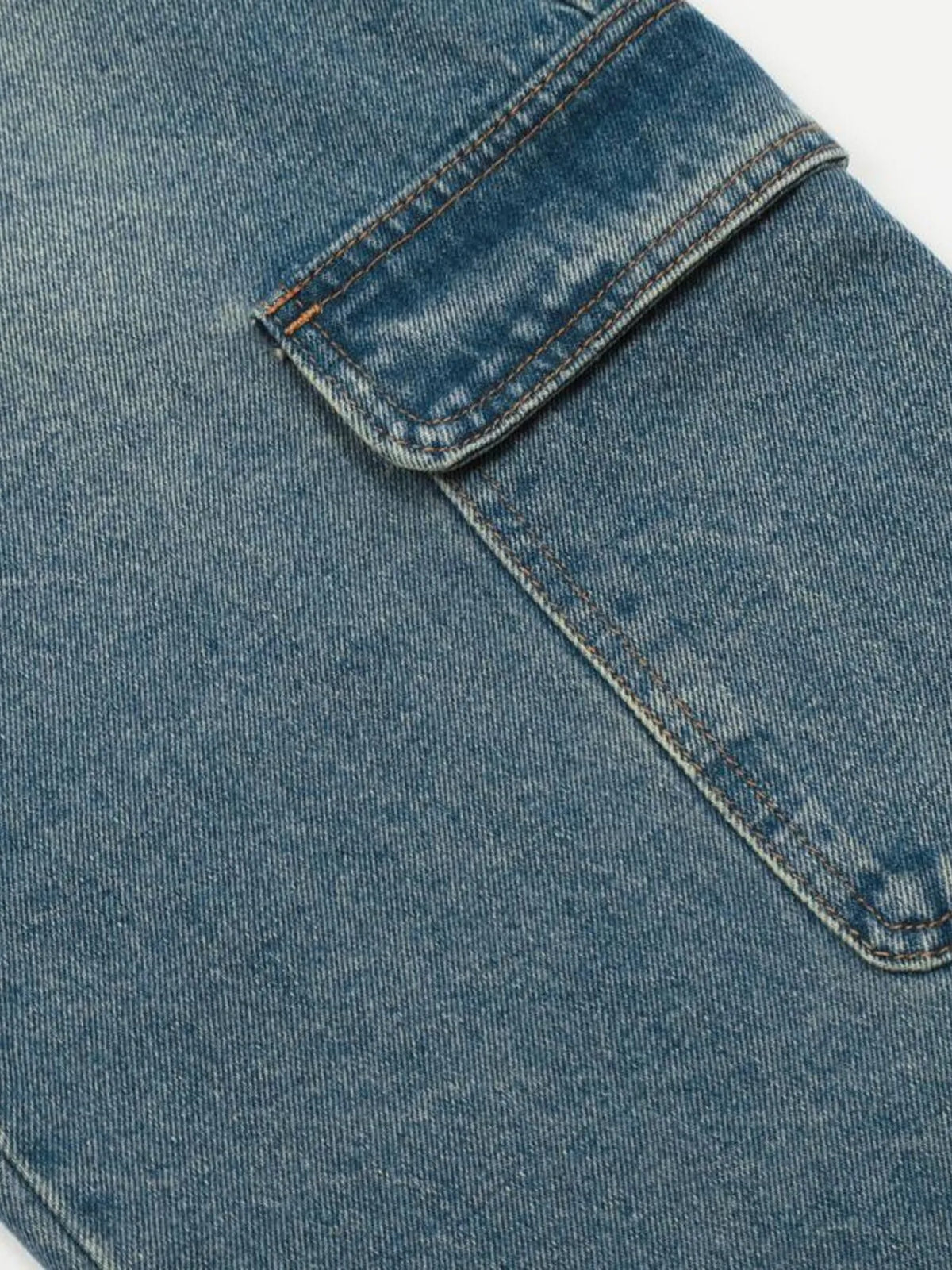 Close-up of a cargo pocket flap and its stitched outline on washed blue denim.