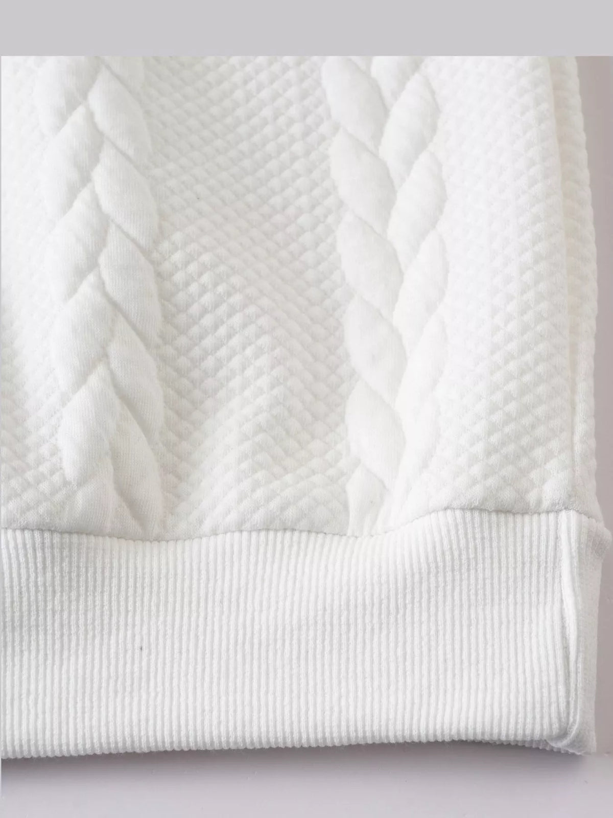 Close view of the white pullover's cable-textured knit and ribbed hem.