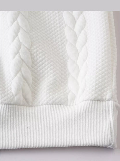 Close view of the white pullover's cable-textured knit and ribbed hem.