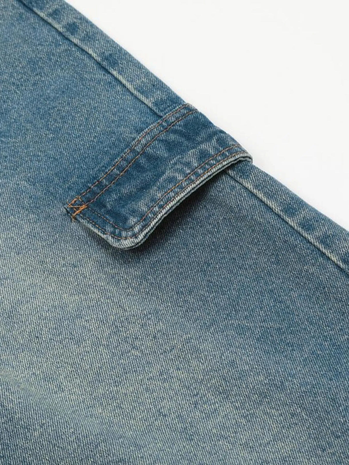 Close-up of the blue denim cargo pocket flap and its fastening area.