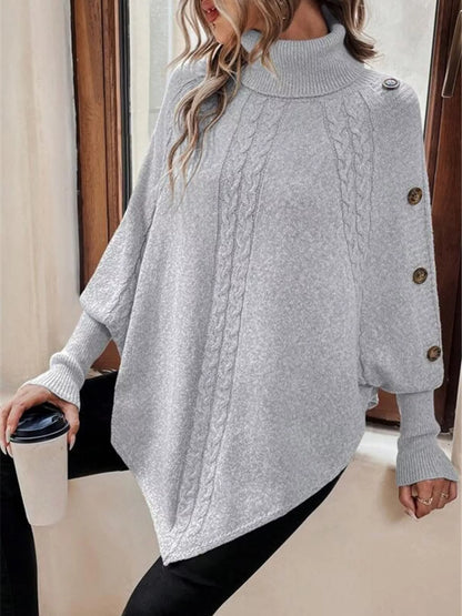 Light gray cable-knit turtleneck cape sweater. Front view, model in black pants. Styling accessories are not included.