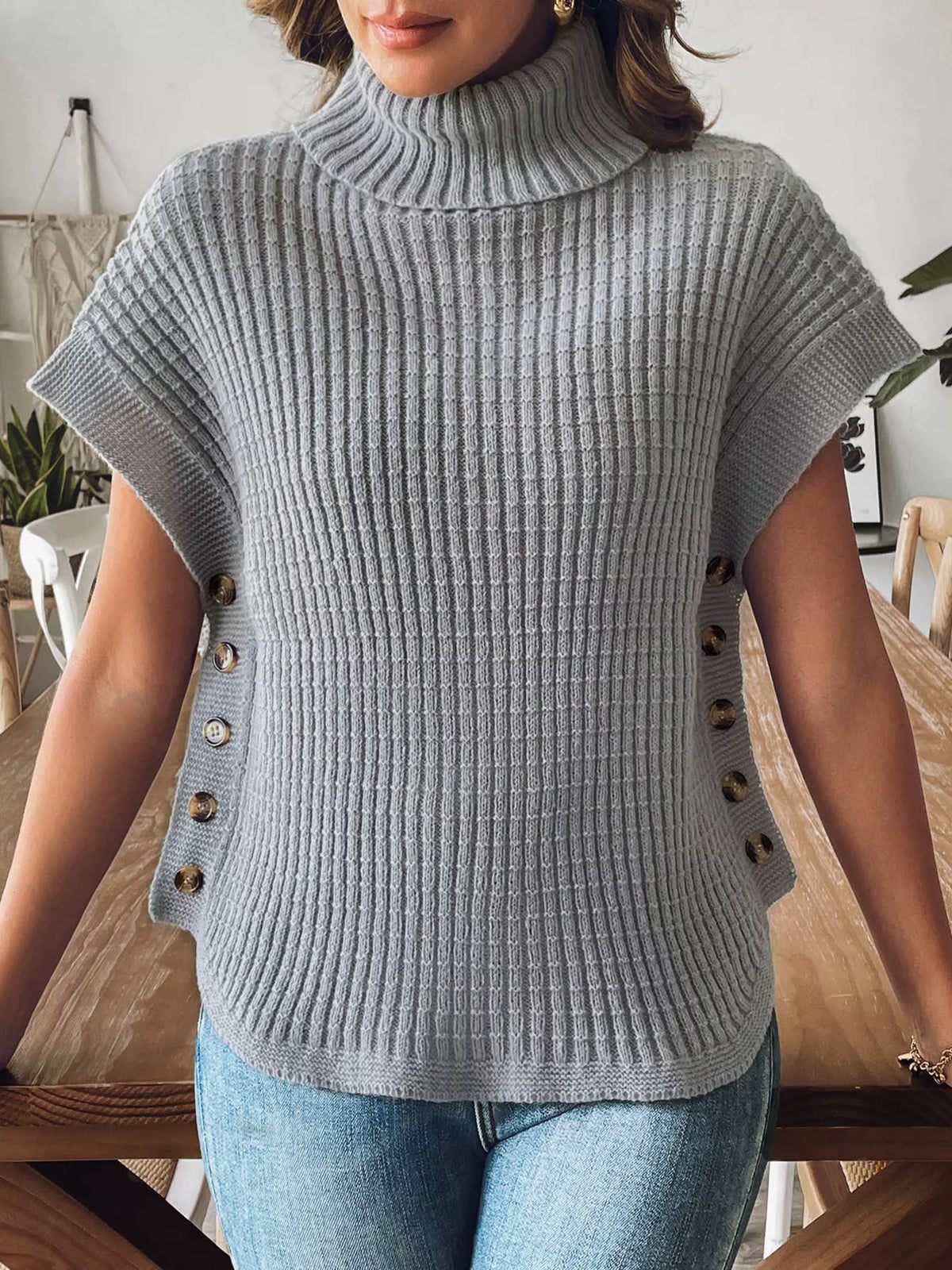 Front view of the grey ribbed turtleneck sweater vest showing the ribbed body and side buttons.