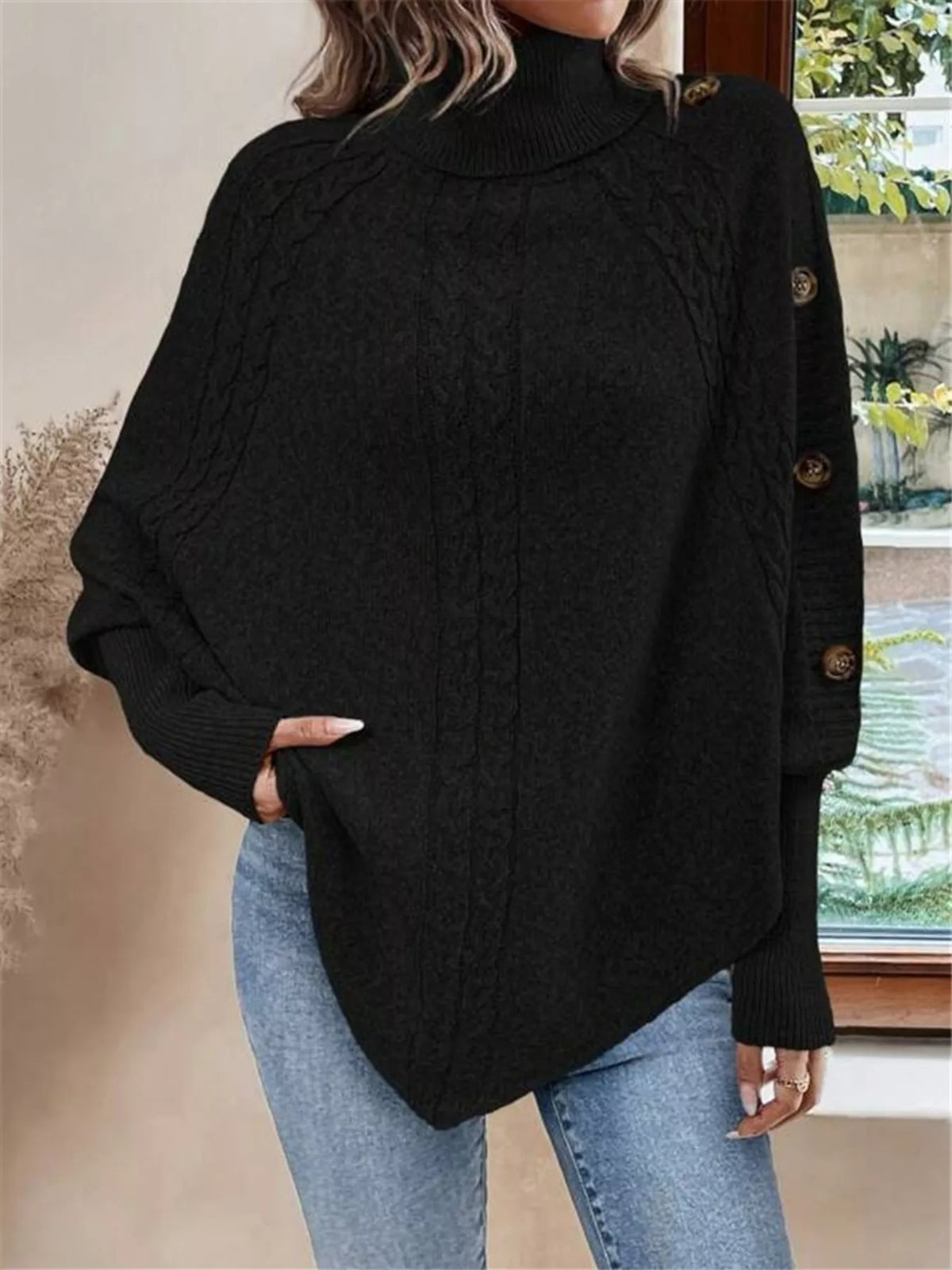 Black cable-knit turtleneck cape sweater. Front detail showing cable knit and shoulder/sleeve buttons. Styling accessories are not included.