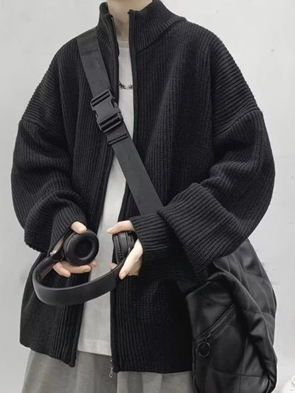 Black oversized ribbed zip-up cardigan worn over a separate light T-shirt, with a bag and headphones used for styling.