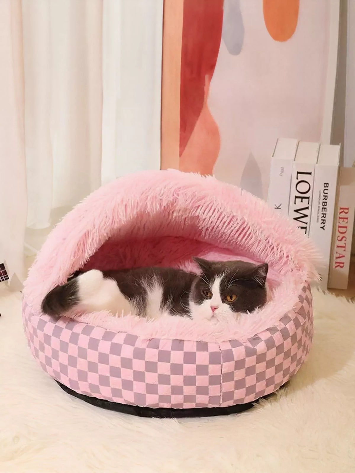 Pink checkerboard covered pet nest with a cat resting inside.