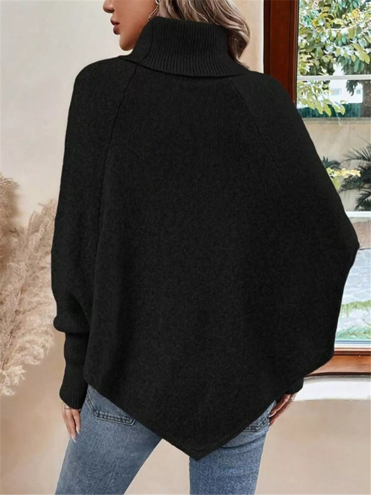 Black cable-knit turtleneck cape sweater. Rear view, model in blue jeans. Styling accessories are not included.