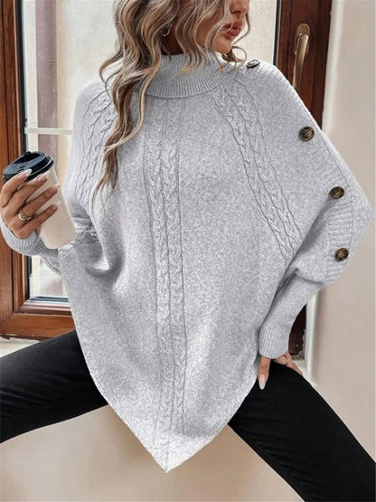 Light gray cable-knit turtleneck cape sweater. Front three-quarter detail showing sleeve buttons. Styling accessories are not included.