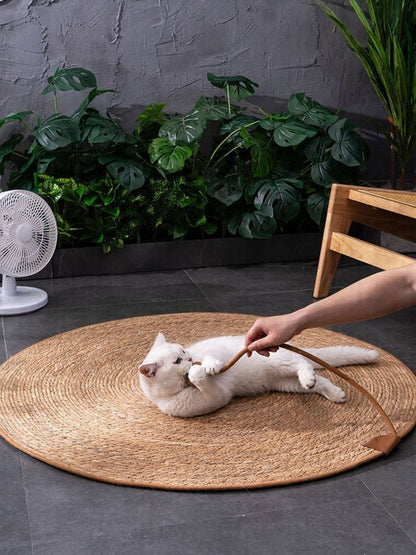 White cat on the round braided pet mat as a hand holds the rope-and-ball detail.