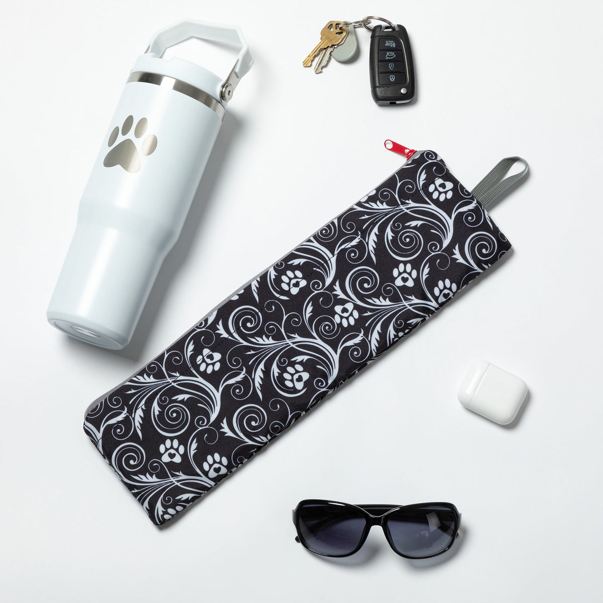 Folded Flourish Paws backpack beside a bottle, sunglasses and small accessories; accessories not included.