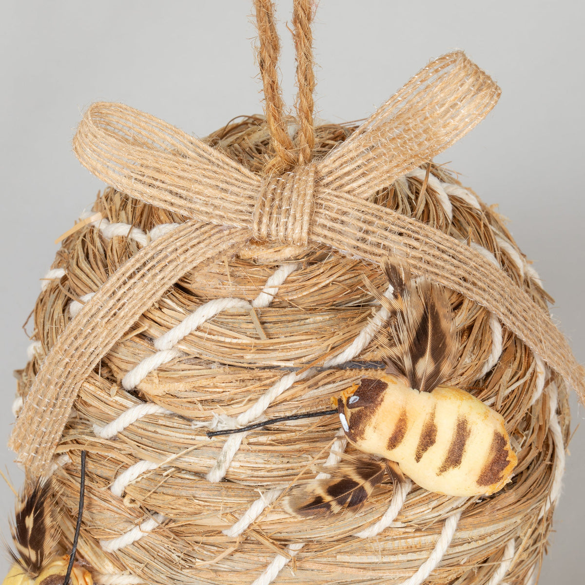 Close-up of the decorative beehive-shaped birdhouse's ribbon and faux bee.