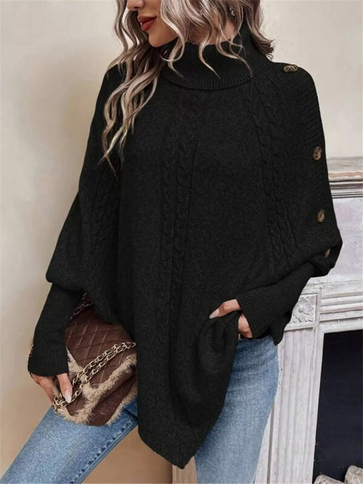 Black cable-knit turtleneck cape sweater. Front view, model in blue jeans. Styling accessories are not included.