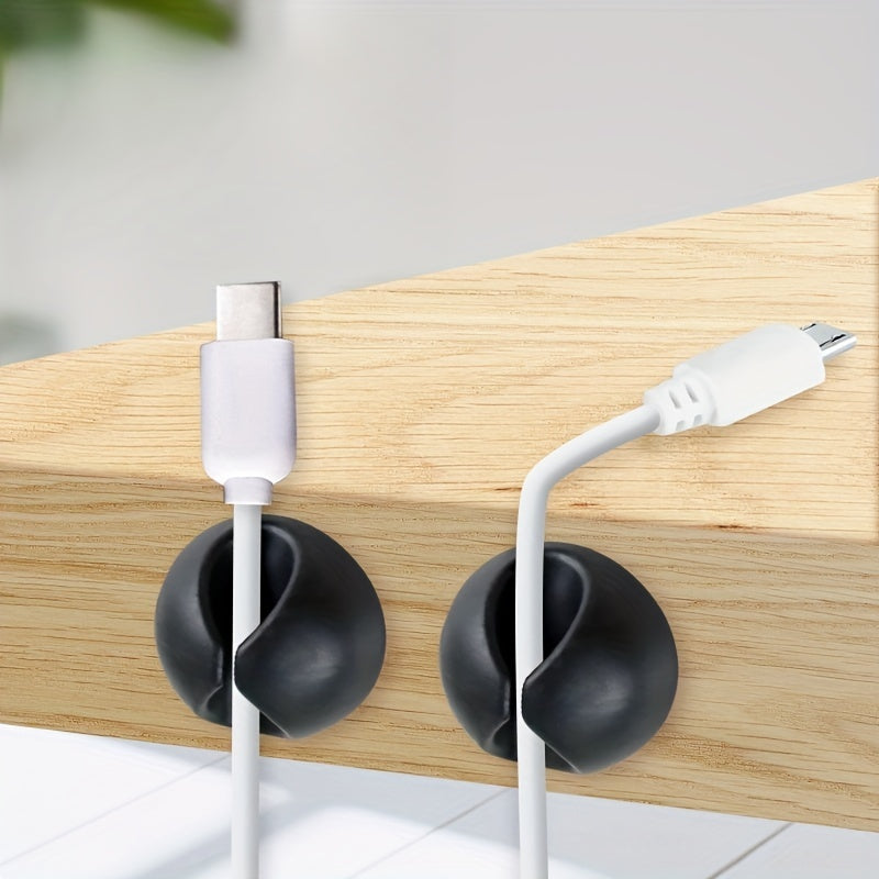 Black cable holders keeping two charging leads at the edge of a desk; cables not included