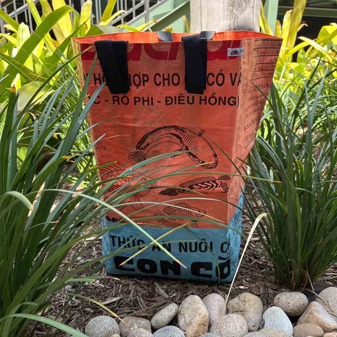 Orange and light blue recycled square laundry bin beside plants; plants are not included.
