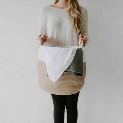 Person holding the cream and beige rope basket with blankets inside; blankets are not included.