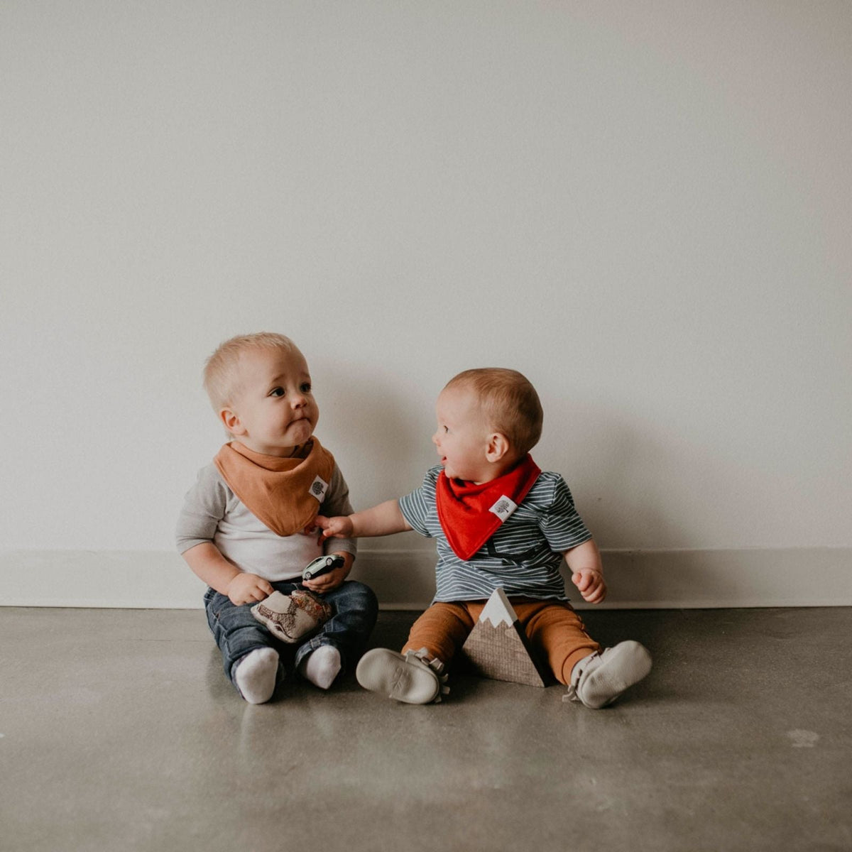 Two babies wearing tan and red bibs from the Estes eight-bib set.