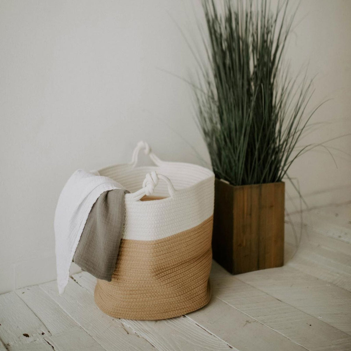 Rope basket holding blankets beside a potted plant; blankets and plant are not included.