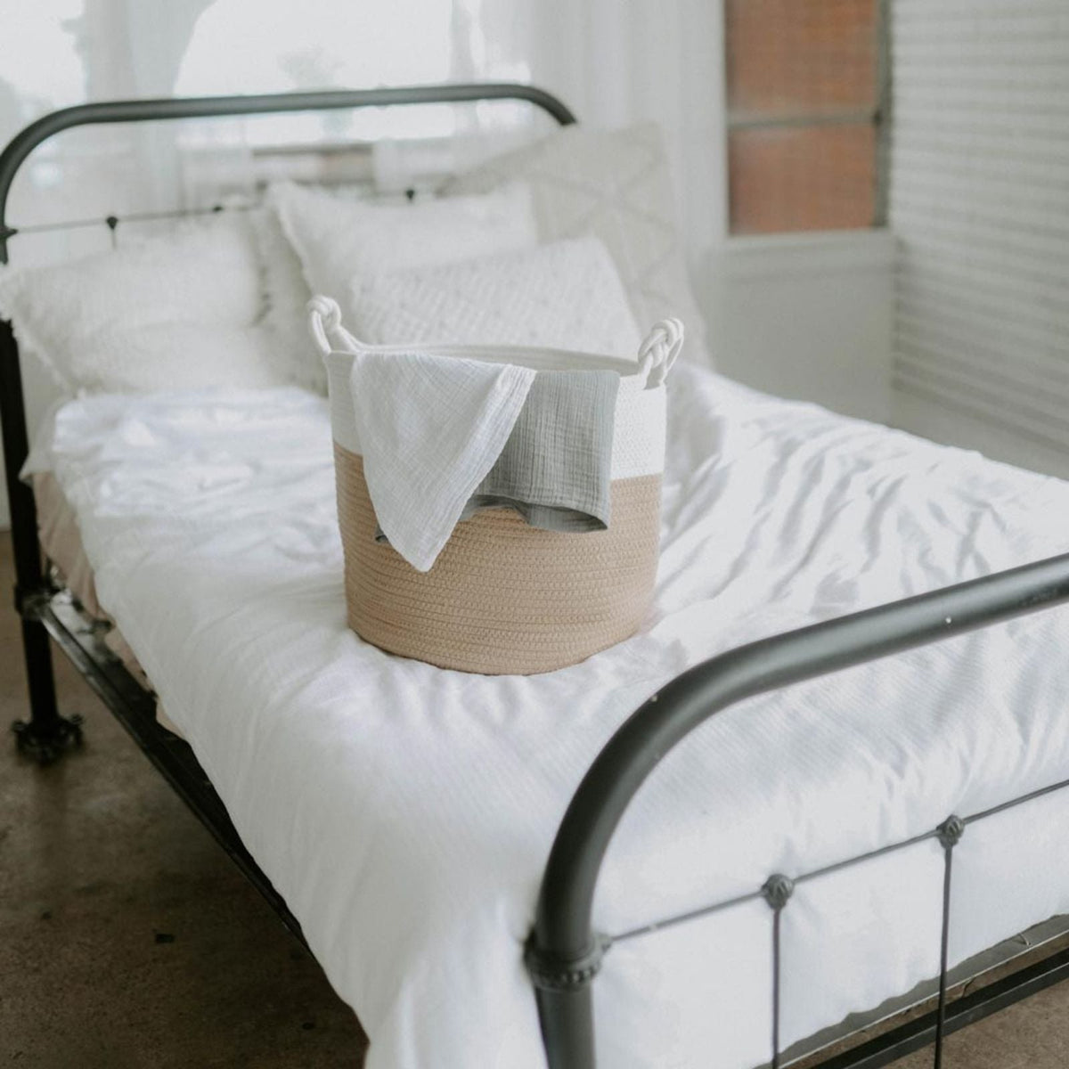 Cream and beige rope basket holding blankets on a bed; bedding is not included.