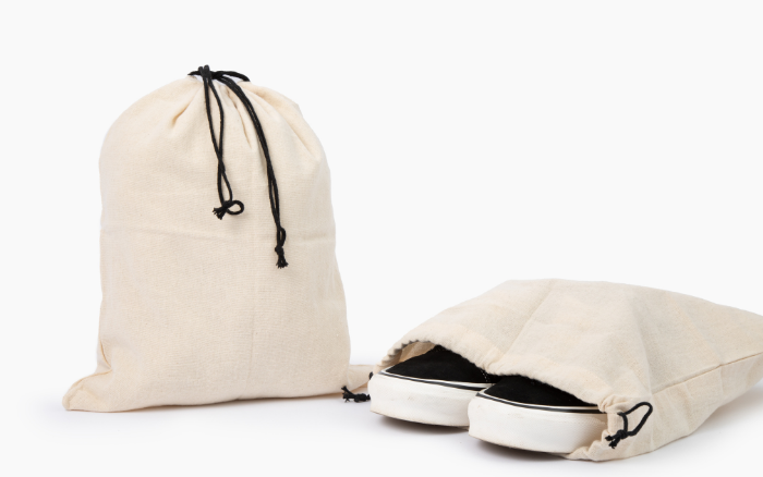 Natural cotton drawstring storage bag beside another holding shoes.
