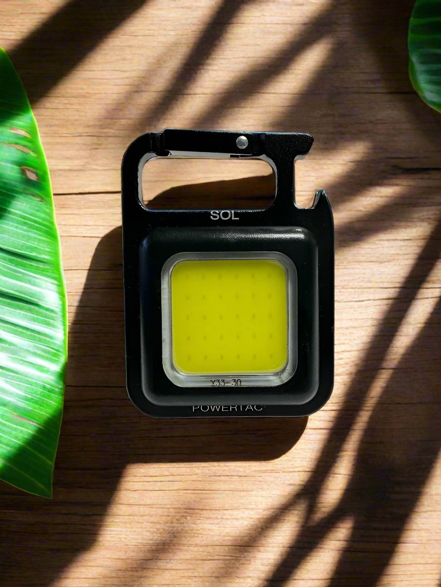 Black Powertac SOL COB keychain light on a wood surface with green leaves.