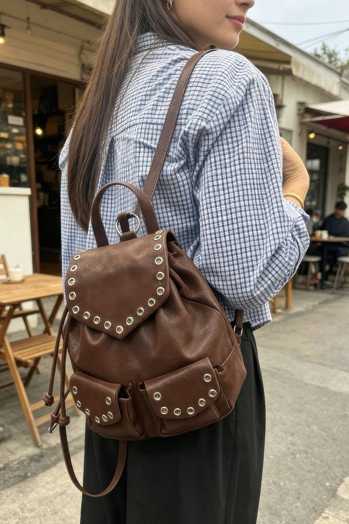 Brown faux-leather backpack worn over one shoulder, showing the curved flap and two front pockets.